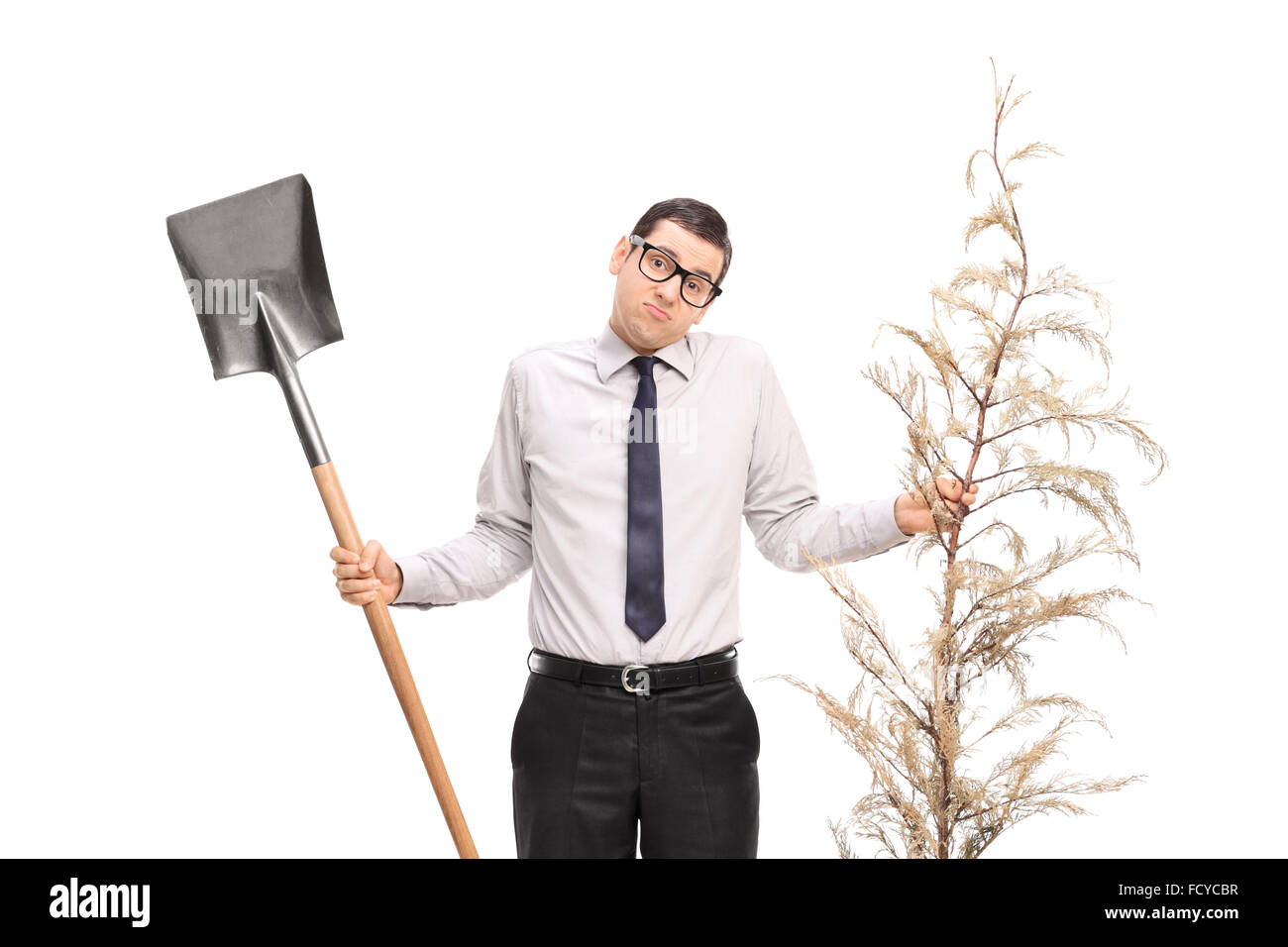 Verwirrt junger Mann hält eine Schaufel und einen ganzen Baum isoliert auf weißem Hintergrund Stockfoto