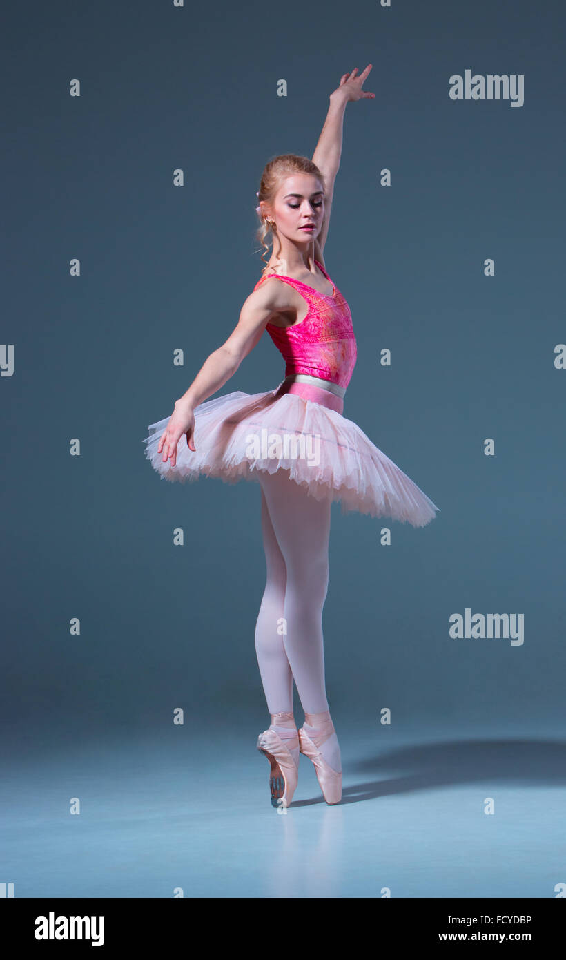 Porträt der Ballerina im Ballett posieren auf einem grauen Hintergrund. Ballerina ist rosa Tutu und Pointe Schuhe tragen. Stockfoto