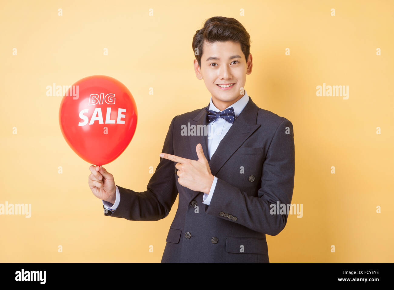Mann in Anzug und Fliege einen großen Verkauf Ballon halten und er mit seinem Finger mit einem Lächeln zu zeigen Stockfoto