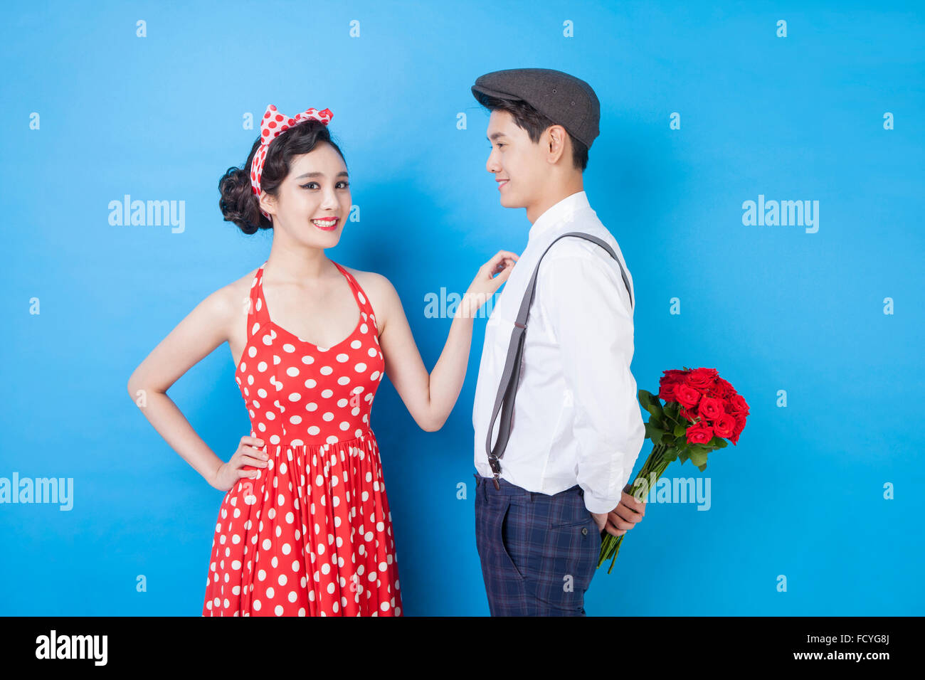 Paar im Retro-Style Mode und Mann hält Rosen hinter seinem Rücken und die Frau mit einem Lächeln betrachten Stockfoto