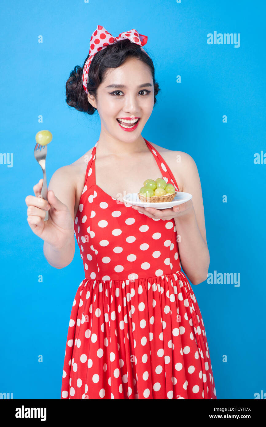 Frau im retro-Stil rot gepunkteten Kleid und Haar Band Halteplatte Traube Teller und Gabel mit einer Traube starrte nach vorne mit Stockfoto
