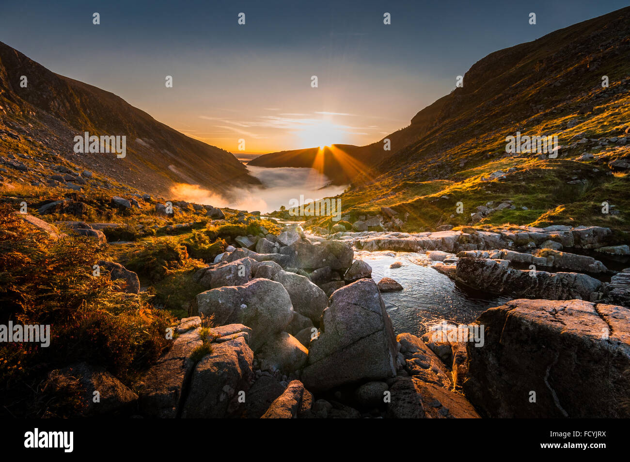 Die Sonne geht mit starken Wellen, goldenes Licht über ein Tal von Glendalough in Wicklow, Irland, die mit niedrigen Wolken gefüllt ist. Stockfoto