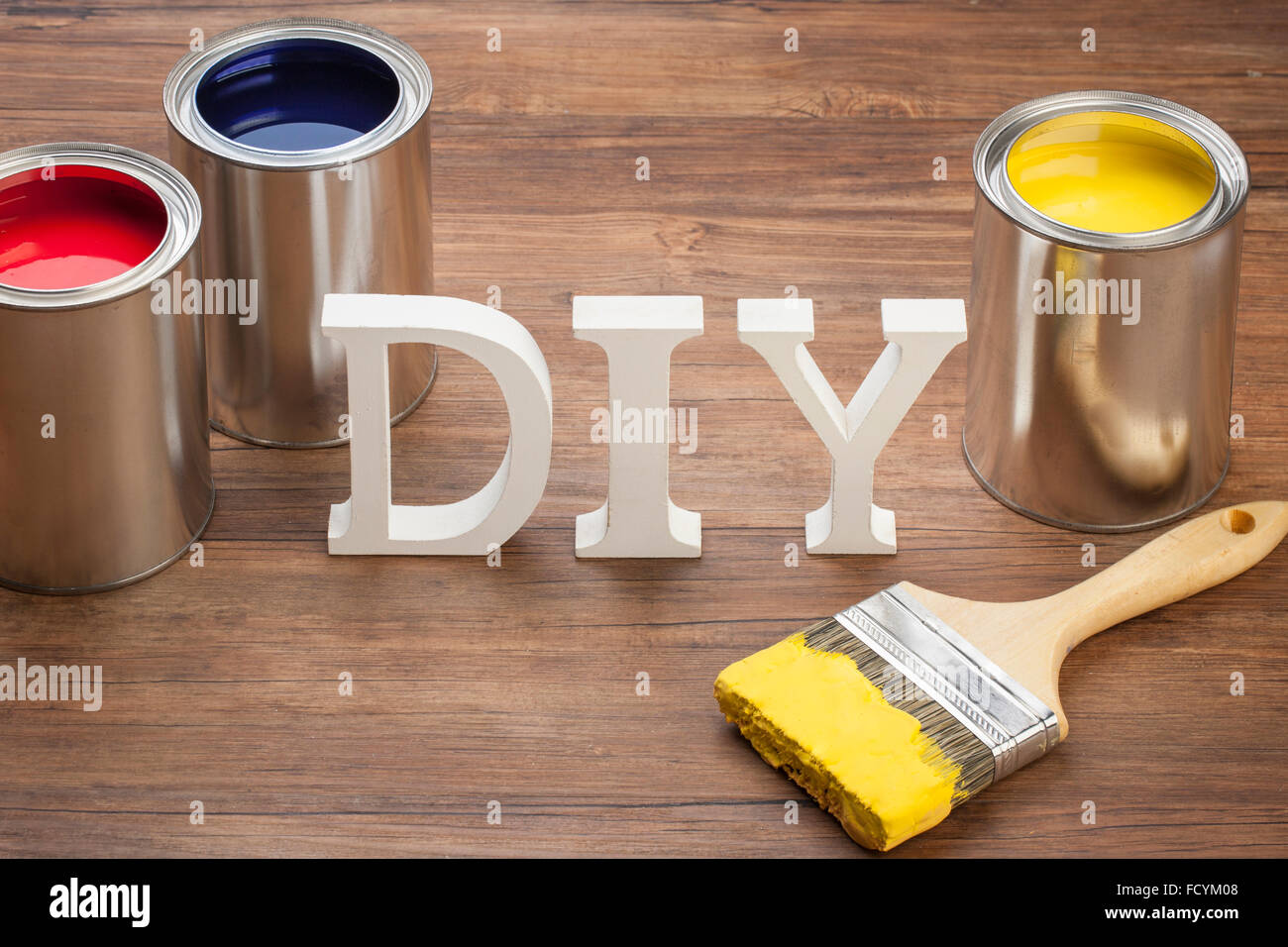 Solide Wort DIY stehend mit drei verschiedenfarbigen Farbtöpfe mit einem Pinsel mit gelber Farbe beschichtet Stockfoto