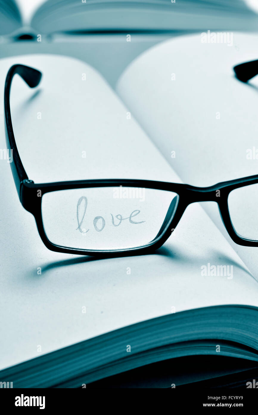 das Wort Liebe in einem Notizbuch, gesehen durch die Linse einer schwarzen Kunststoff-umrandeten Brille in Duotone handschriftliche Stockfoto