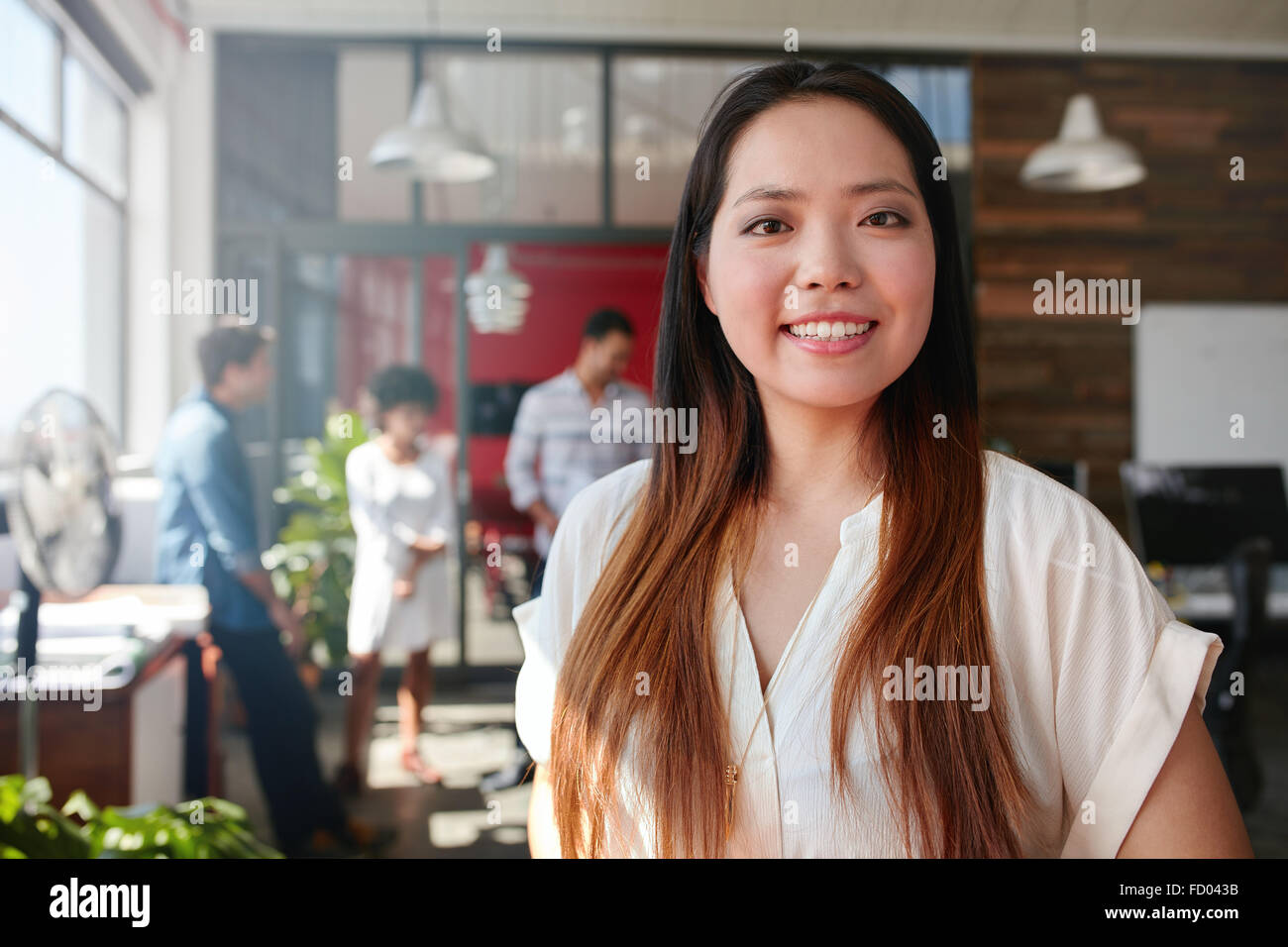 Lächelnde junge Geschäftsfrau Blick auf Kamera und ihre Kollegen stehen im Hintergrund. Junge asiatische Frauen kreative pro Stockfoto