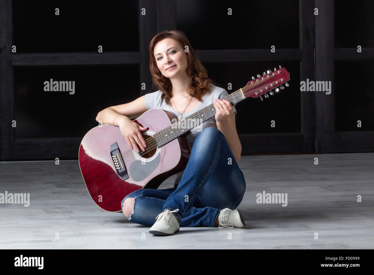 Mädchen mit Gitarre auf dem Boden sitzend Stockfoto