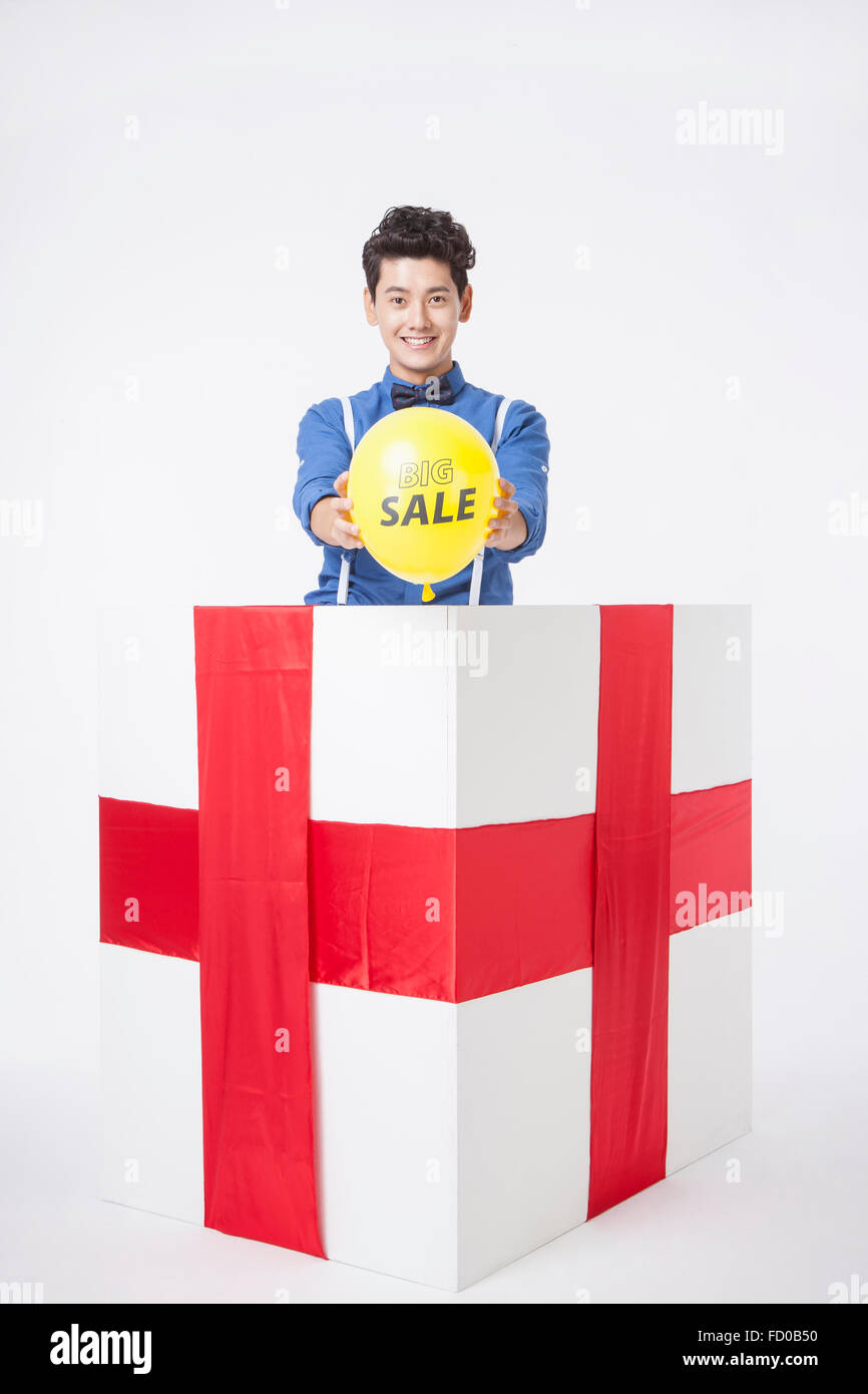 Mann im blauen Hemd in einer Geschenkbox starrte nach vorne und halten eine Sprechblase mit Verkaufsschild nach vorne platziert Stockfoto