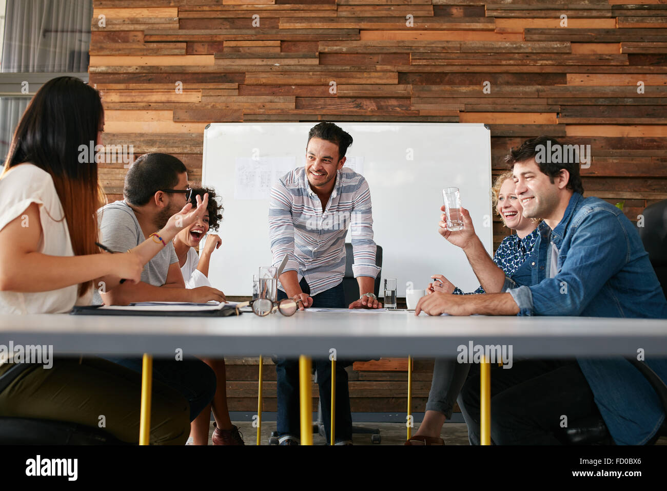 Gruppe der glückliche junge Menschen, die ein Business-Meeting. Kreative Leute sitzen am Tisch im Sitzungssaal mit Mann erklären busines Stockfoto