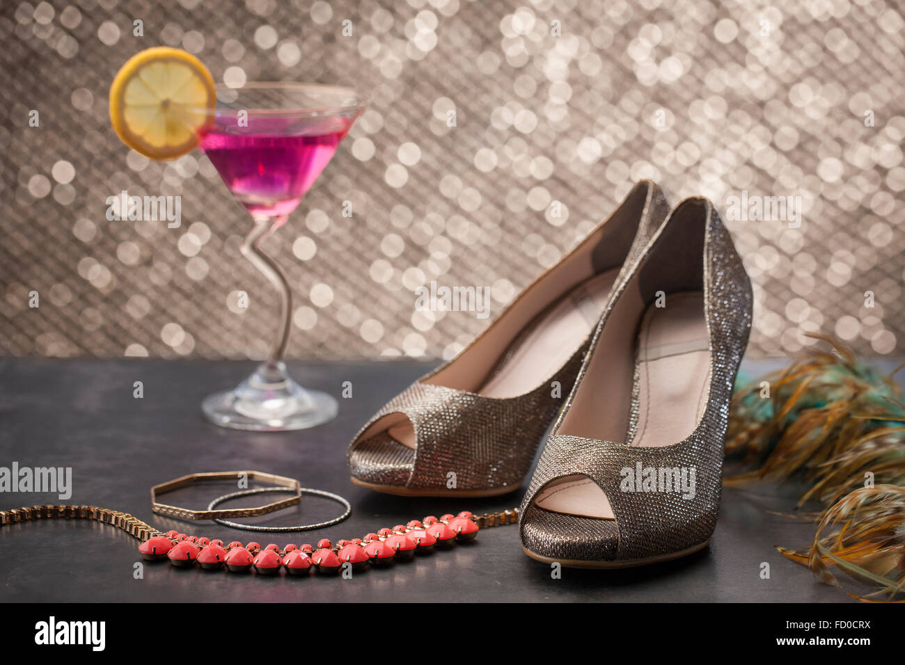 Glitzernden high Heels auf Tisch mit Armbänder und ein Glas cocktail Stockfoto
