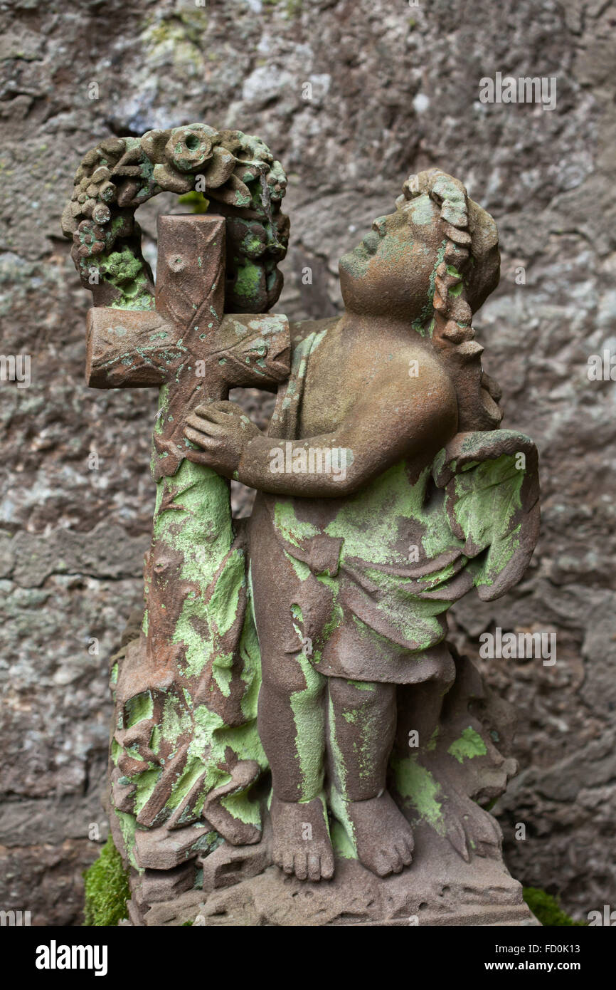 Engel mit einem Kreuz bedeckt mit Moos. Statuette auf dem Kirchhof in Creglingen, Baden-Württemberg, Deutschland. Stockfoto