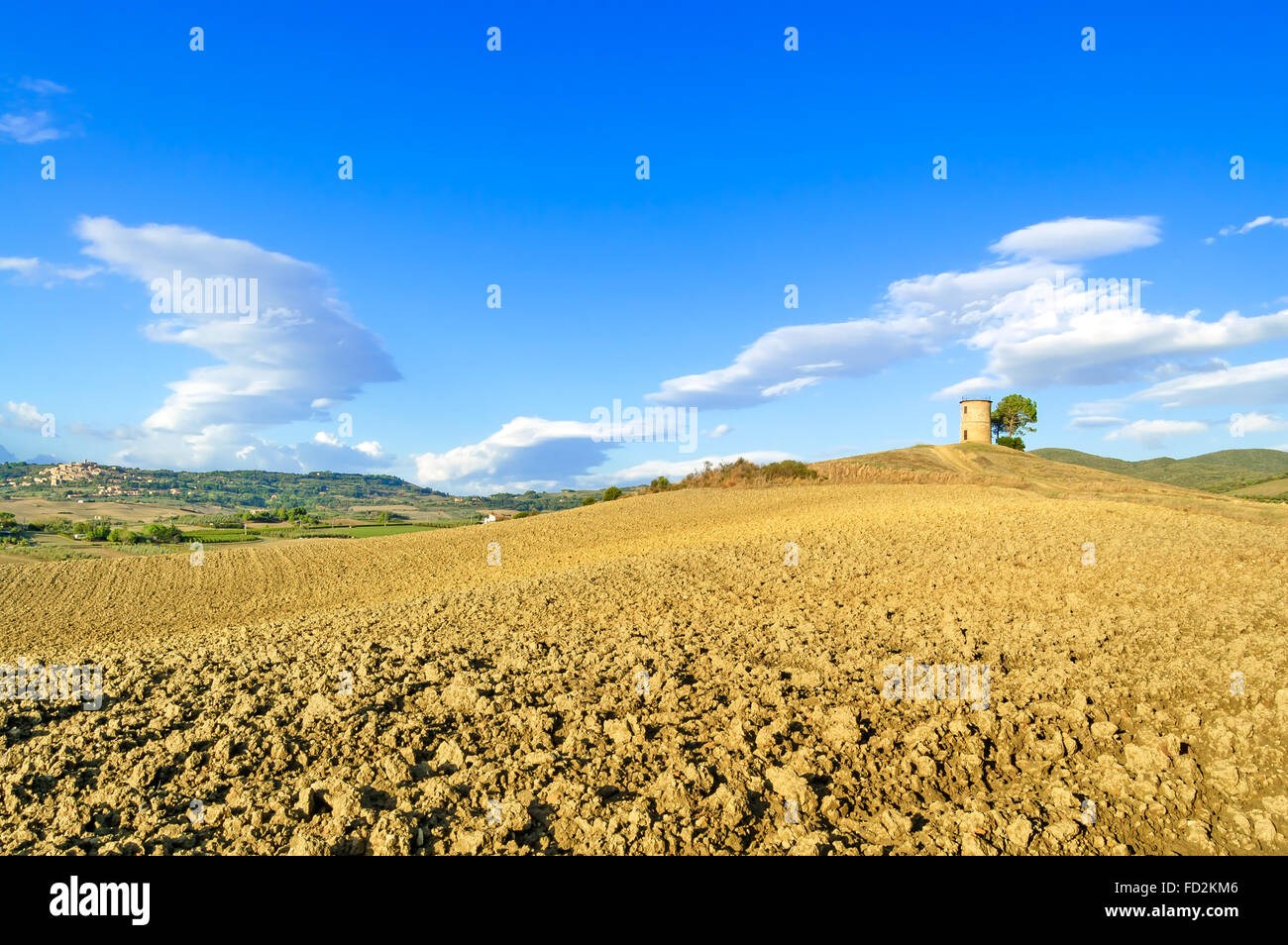 Toskana Maremma typische Landschaft mit sanften Hügeln, ländlichen Turm, gepflügtes Feld und Dorf im Hintergrund. Stockfoto