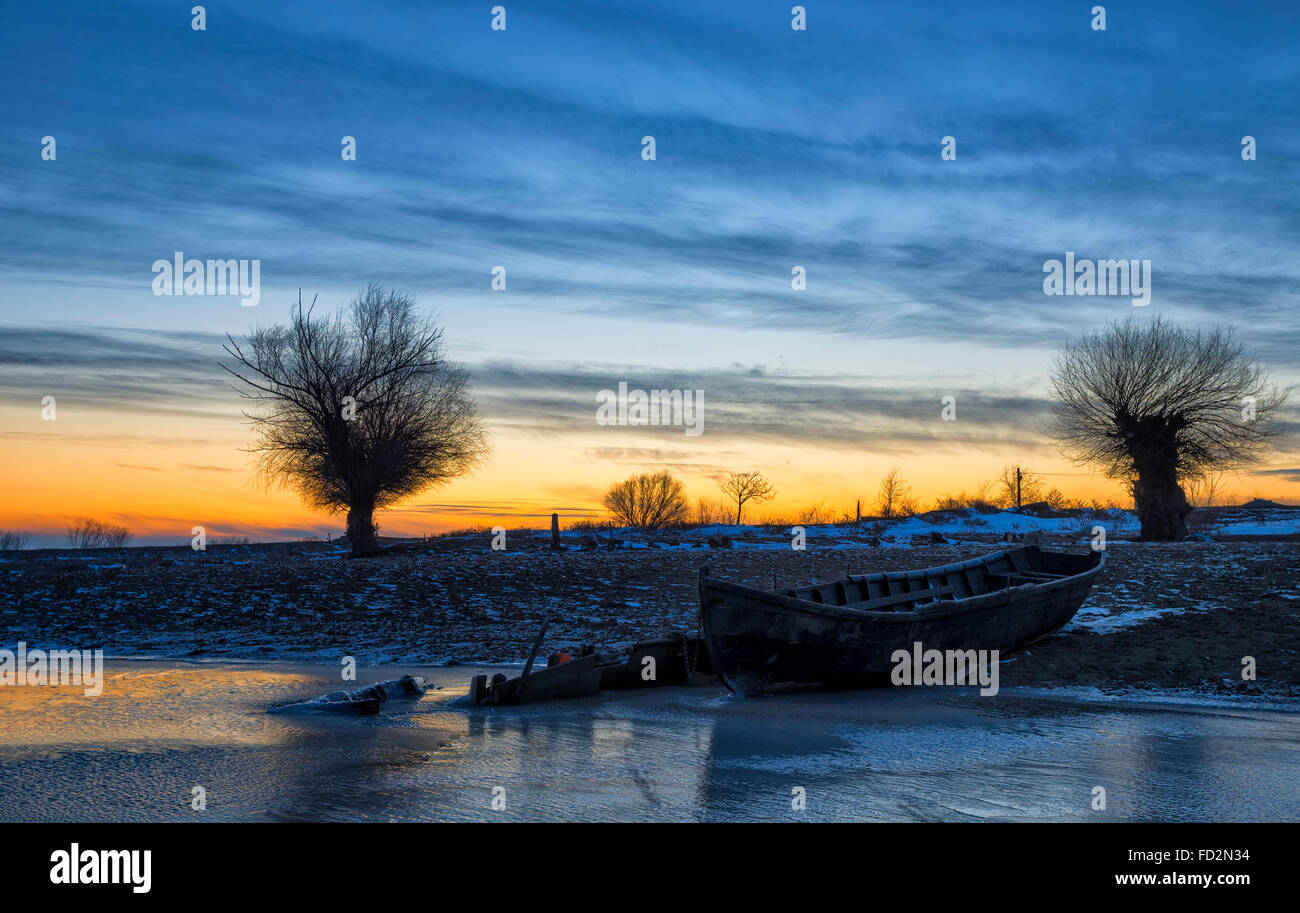 altes Boot bei Sonnenuntergang an der Donau im winter Stockfoto