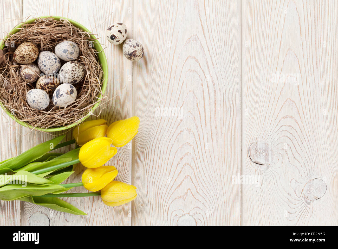 Ostern-Hintergrund mit Eiern im Nest und gelbe Tulpen in weißer Holztisch. Ansicht von oben Stockfoto