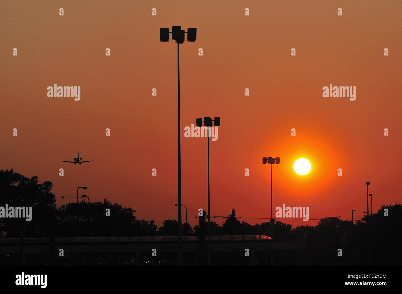 Ein Strahl auf den Endanflug weg zu Land fliegt in die untergehende Sonne am Chicago O'Hare International Airport entfernt. Chicago, Illinois, USA. Stockfoto