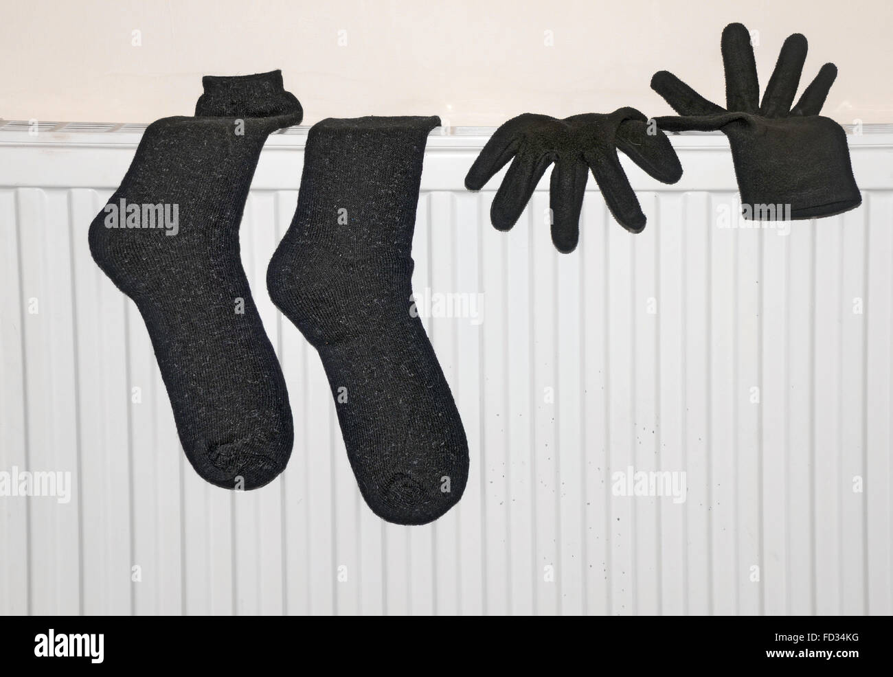 ein schwarzes paar nasse Handschuhe und Socken Trocknen auf einem Heizkörper in einem Raum. Stockfoto