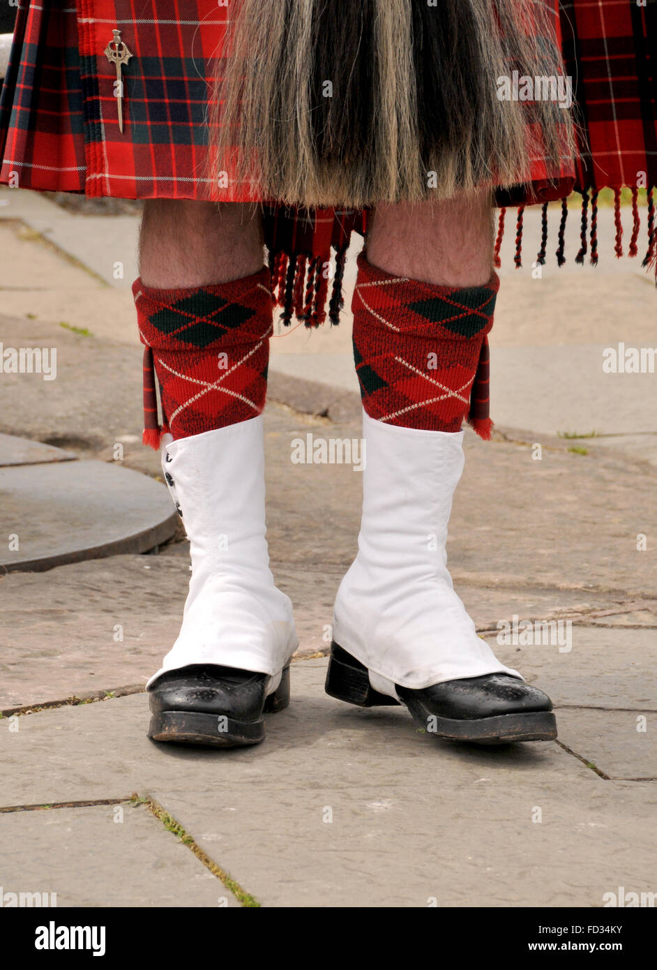 Beine und Schuhe von einem ständigen schottischen Mann gekleidet in einen roten aufgegebenes Tartan Kilt. Stockfoto