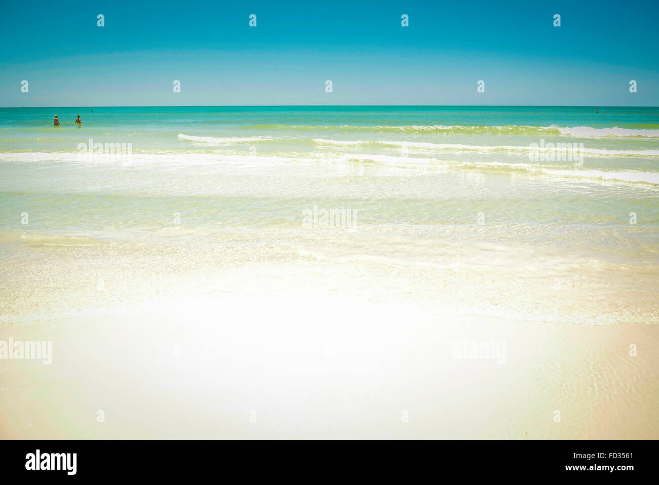 Eine Weitwinkelaufnahme einen idyllischen weißen Sandstrandes mit Surf und blauen Seelandschaft und fernen Menschen tummeln sich in den sanften Wellen Stockfoto