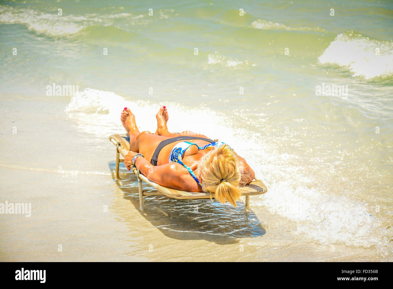 Eine Solo Frau liegt Gesicht oben und horizontal auf den Strand liegen umgeben von den sanft brechenden Wellen der Brandung am Strand Stockfoto
