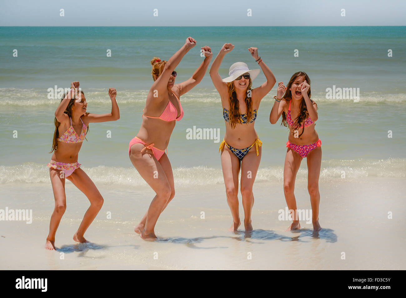 Vier jubelnde Frauen in Bikinis zu feiern, lachen und Ausgelassenheit in der Brandung am Strand Stockfoto