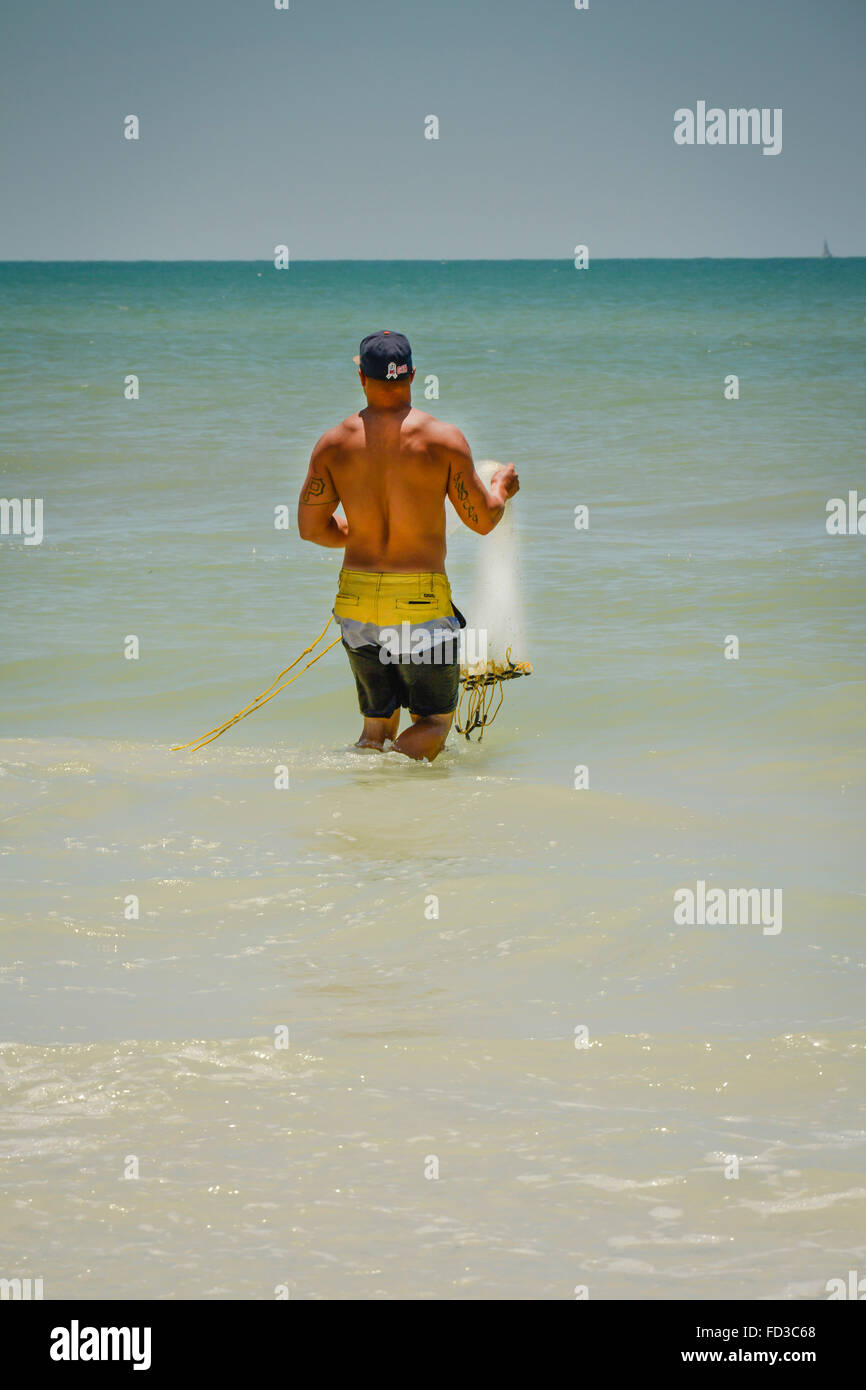 Eine Rückansicht eines einsamen tätowierten Mannes in bunte Badehose vorbereiten, ein Netz für das Fischen in Taille Tiefenwasser in der Golfregion zu werfen Stockfoto