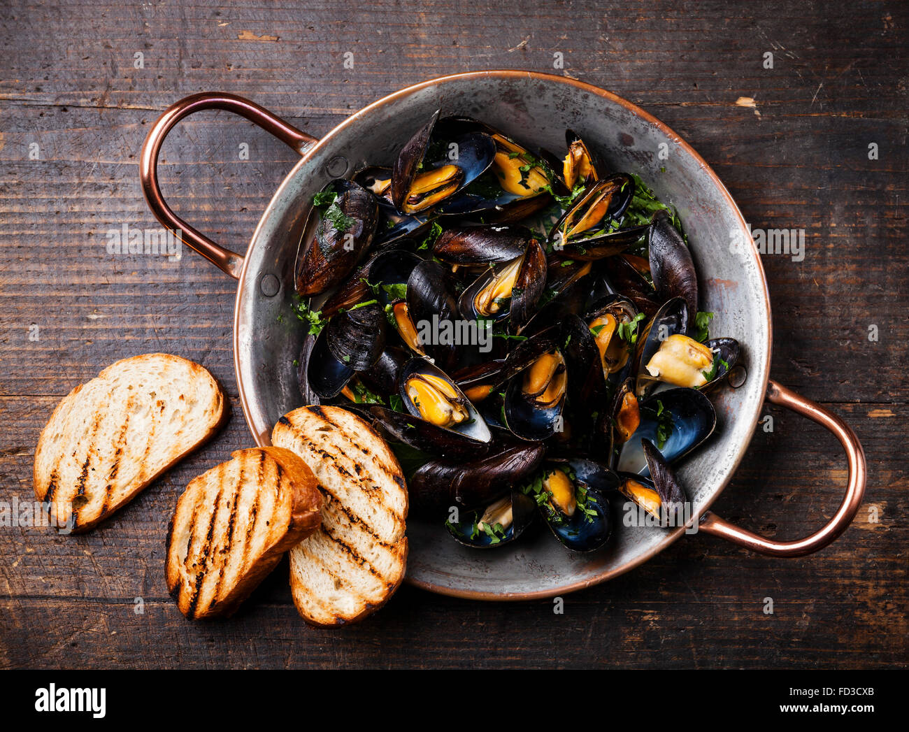 Muscheln in Kupfer Kochen Schüssel und Brot Toasten auf dunklem Holz Stockfoto