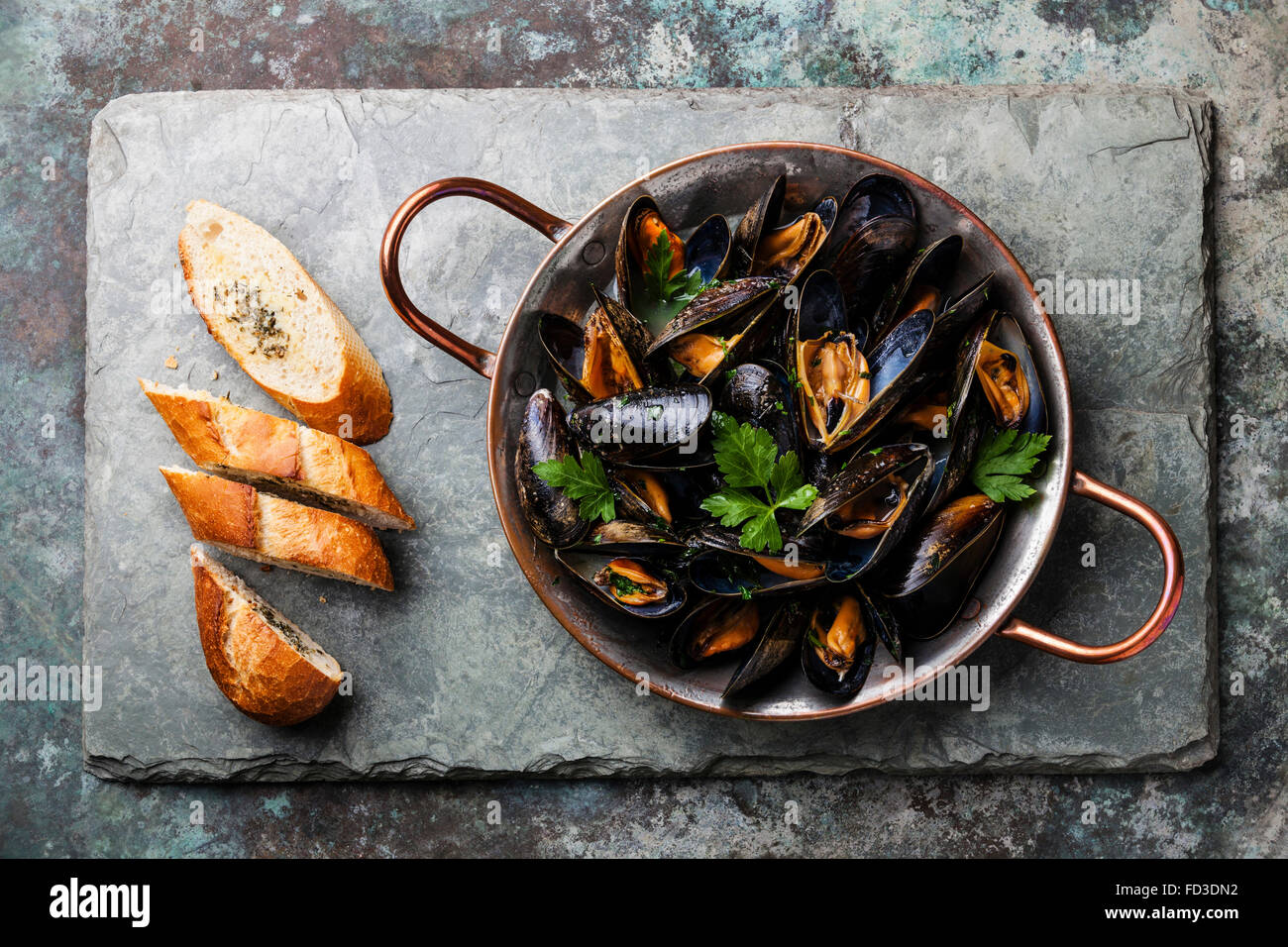 Muscheln in Kupfer Kochen Schüssel und französische Baguette mit Kräutern auf Stein Schiefer Hintergrund Stockfoto