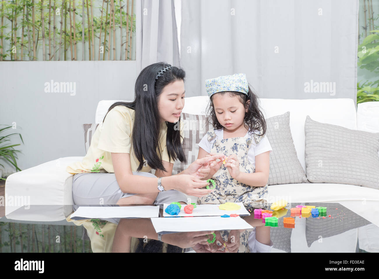 Familie, Kinder und glückliche Menschen Konzept - asiatische Mutter und Kind Tochter spielt mit Plastilin in Haus Stockfoto
