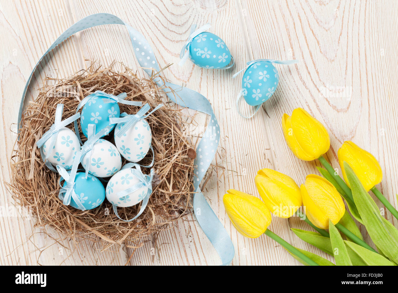 Ostern-Hintergrund mit Eiern im Nest und gelbe Tulpen in weißer Holztisch. Ansicht von oben Stockfoto