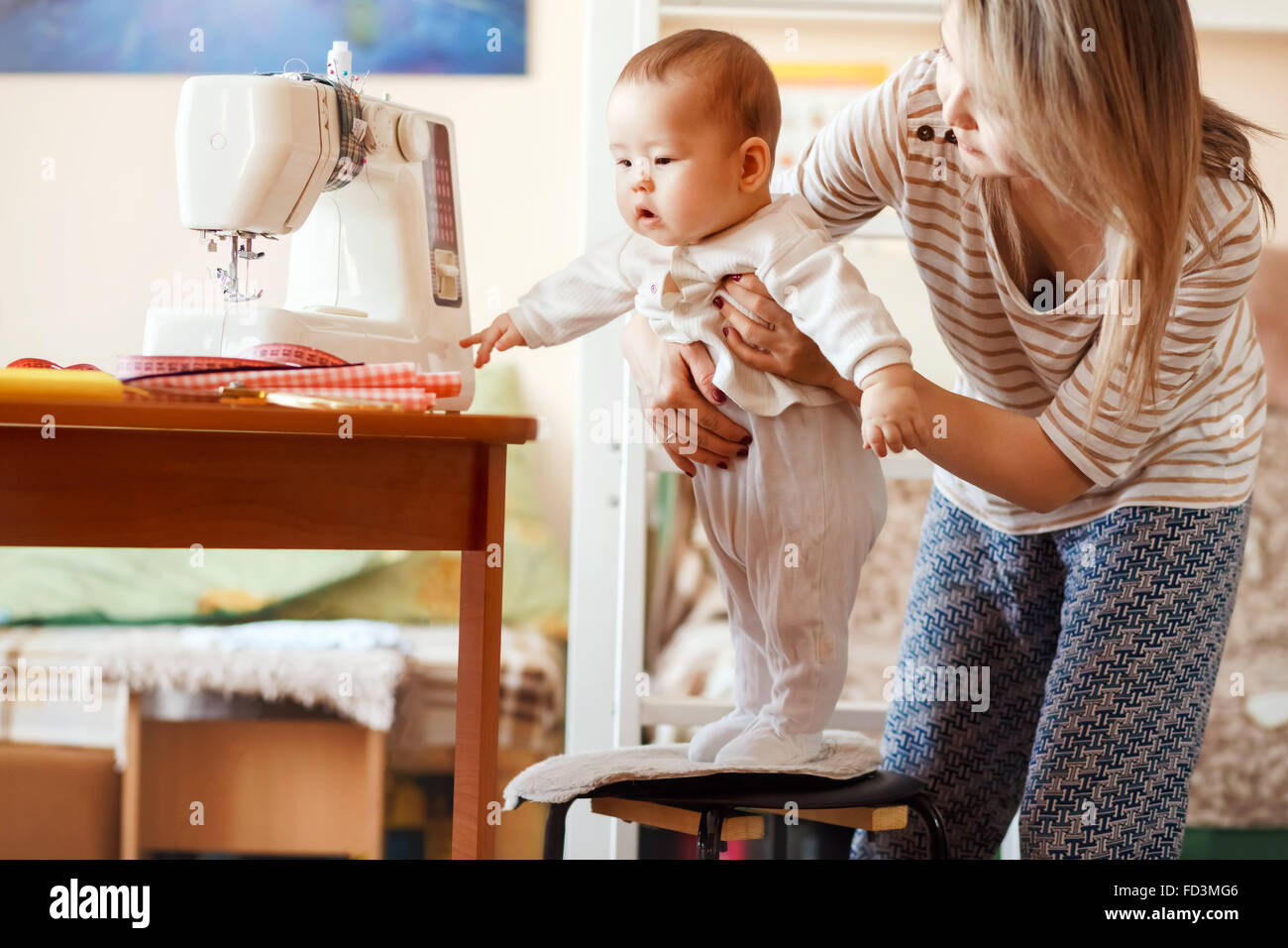 Mutter und Kind, zu Hause, die erste Gehversuche, natürliches Licht. Baby-/Kinderbetreuung kombiniert mit Arbeit zu Hause. Stockfoto