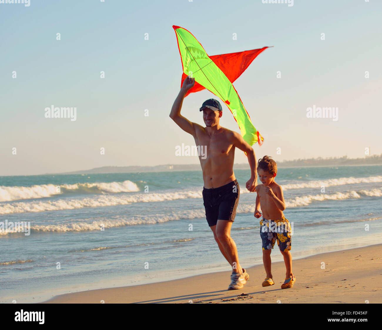 Vater mit Sohn, Sonnenuntergang an der Küste mit Drachen, glückliche Familie Stockfoto