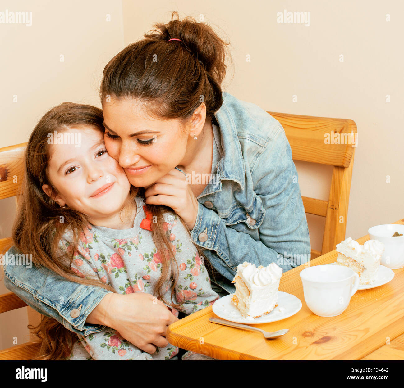 junge Mutter mit Tochter in der Küche Tee zusammen umarmt Feier Kuchen essen trinken Stockfoto