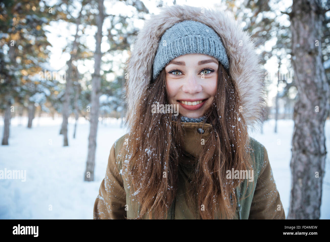 Porträt von lächelnden hübsche junge Frau in warme Mütze und Jacke mit Kapuze in Winter park Stockfoto