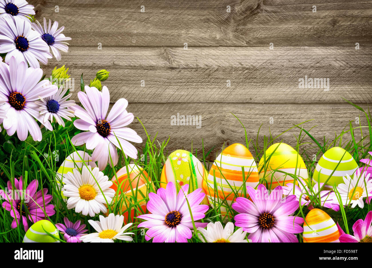 Frühlingsblumen und glücklich bunte Ostereier mit rustikalen hölzernen Planken im Hintergrund Stockfoto