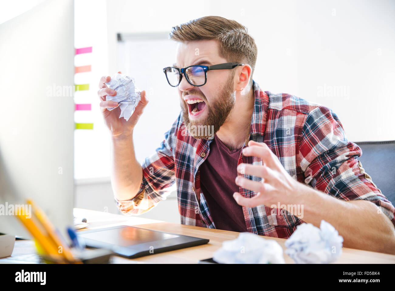 Wütend verrückt moderne Designer in Gläsern mit Bart schreien und zerknitterte Papier auf seinem Arbeitsplatz Stockfoto