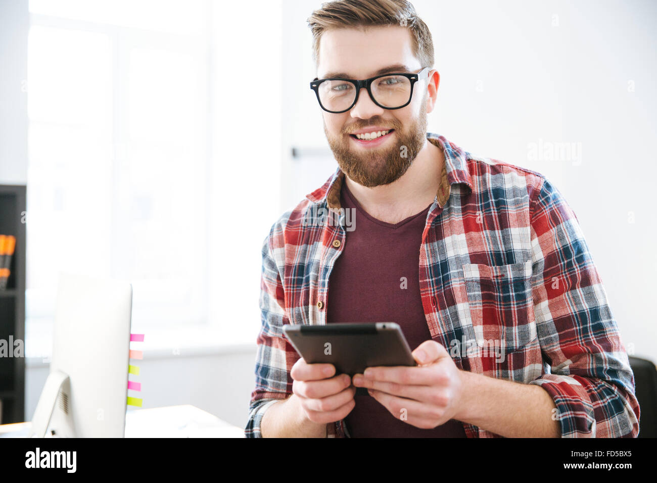 Glücklich gut aussehend bärtiger Mann in Gläsern mit Tablet im Büro Stockfoto