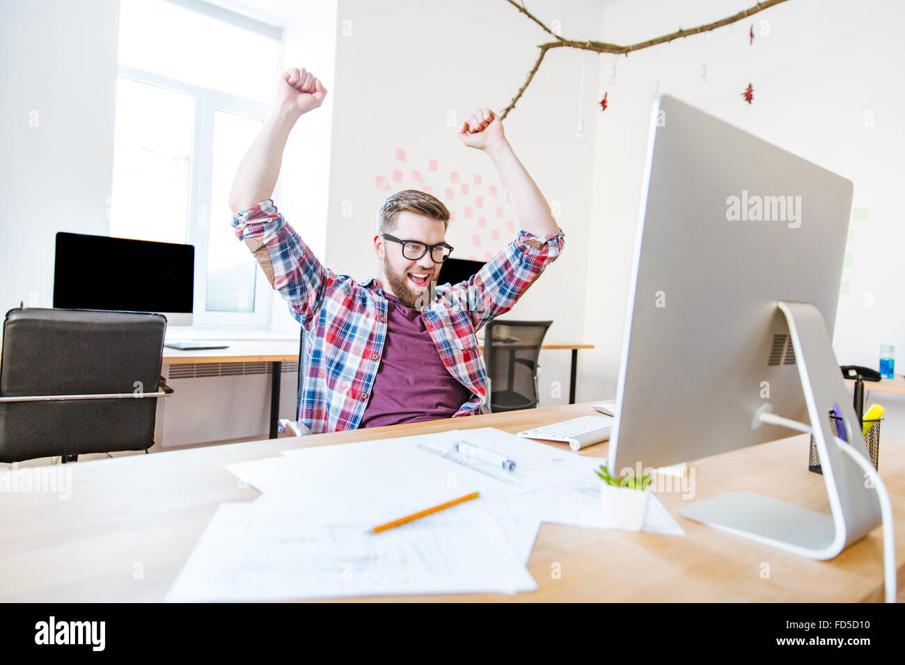 Erfolgreiche glücklich in Gläsern mit erhobenen Händen sitzen am Arbeitsplatz im Büro Stockfoto
