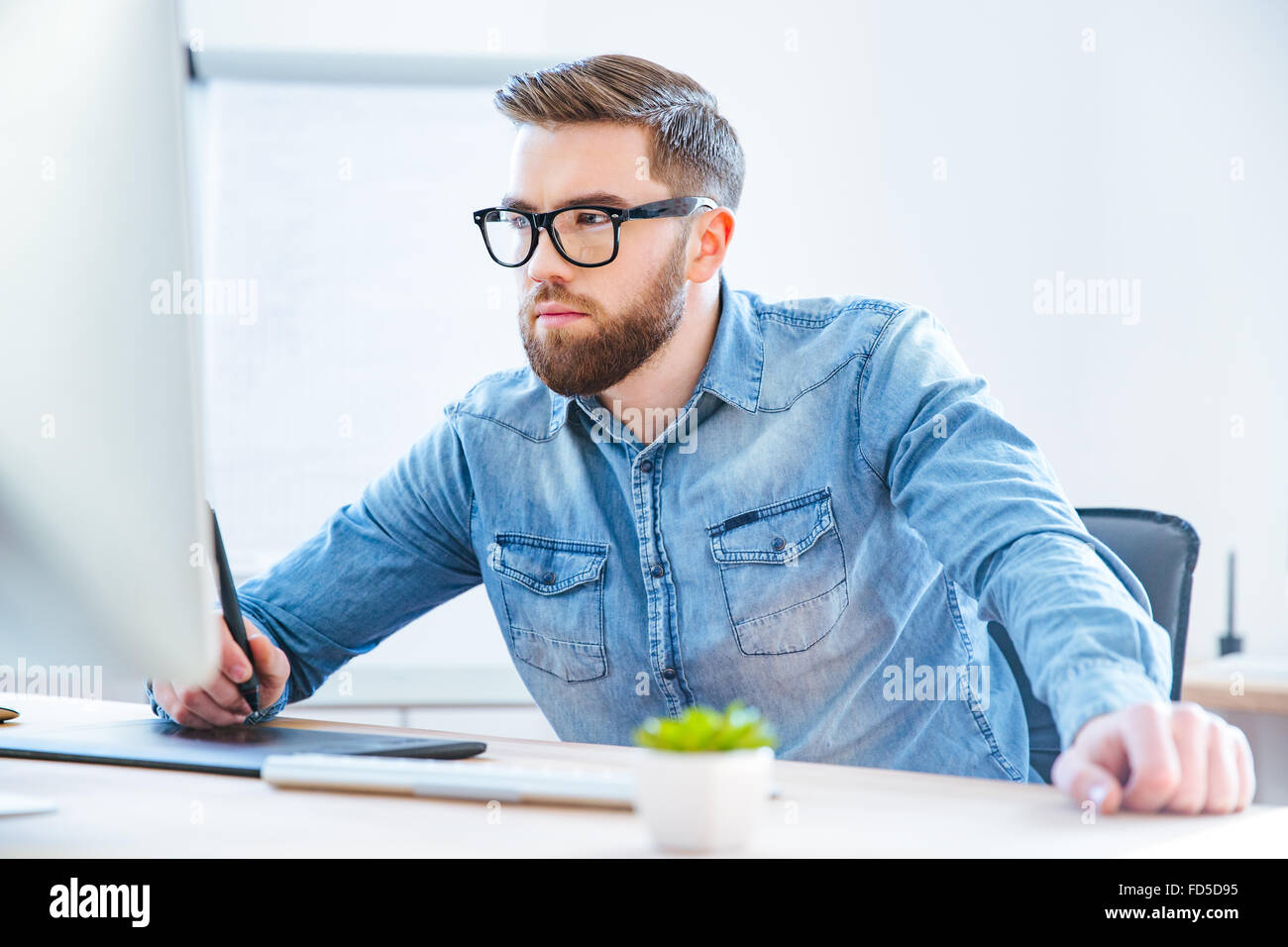 Ernsthafte konzentrierte Jüngling Designer-Zeichnung mit Grafik-Pen Tablet mit Stylus im Büro Stockfoto