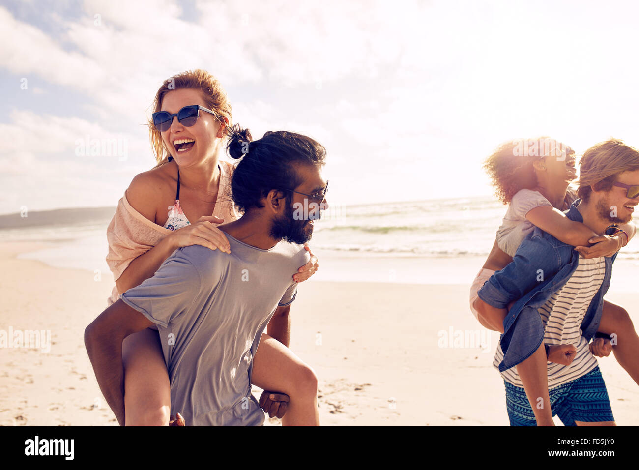 Glückliche junge Männer geben Huckepack Fahrt für Frauen am Strand. Heterogene Gruppe von jungen Leuten, die Spaß am Strand und Huckepack. Stockfoto