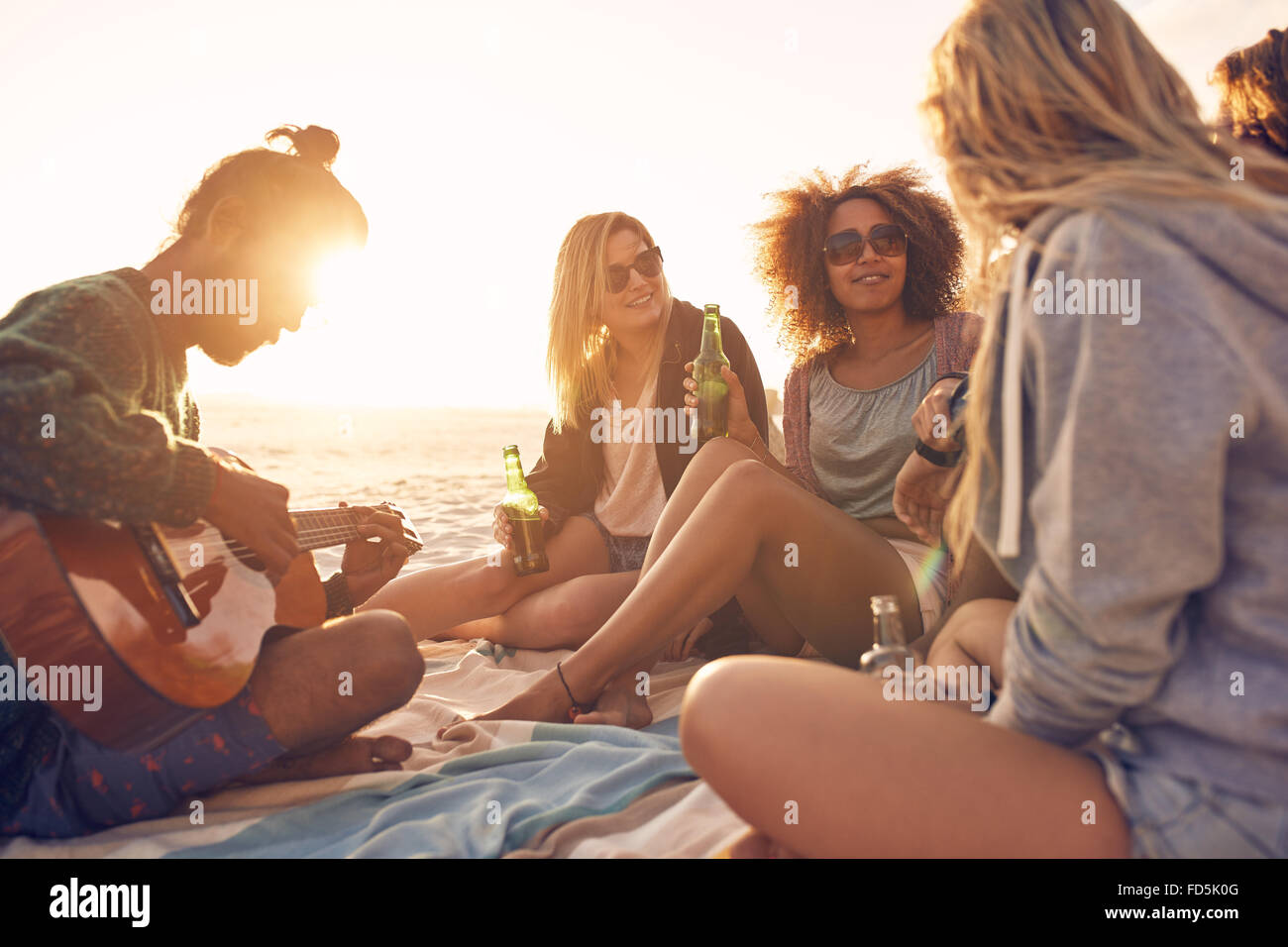 Gruppe von jungen Leuten am Strand beisammen sitzen, während der junge Mann, die Gitarre zu spielen. Gruppe von Freunden feiern am Strand von su Stockfoto