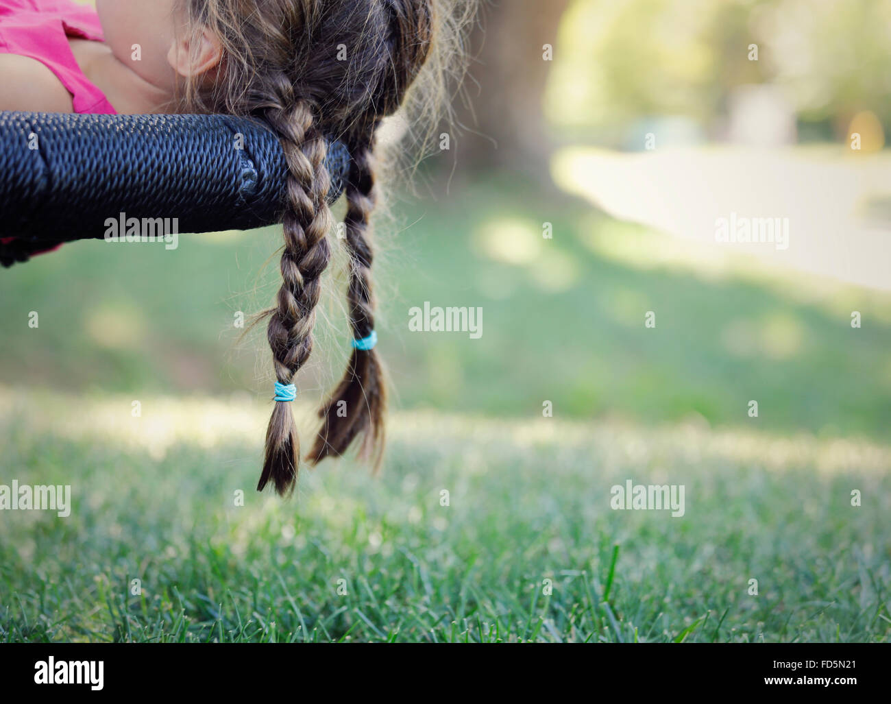 Bild von eines jungen Mädchens Zöpfe hängen über den Rand ihrer Schaukel. Stockfoto