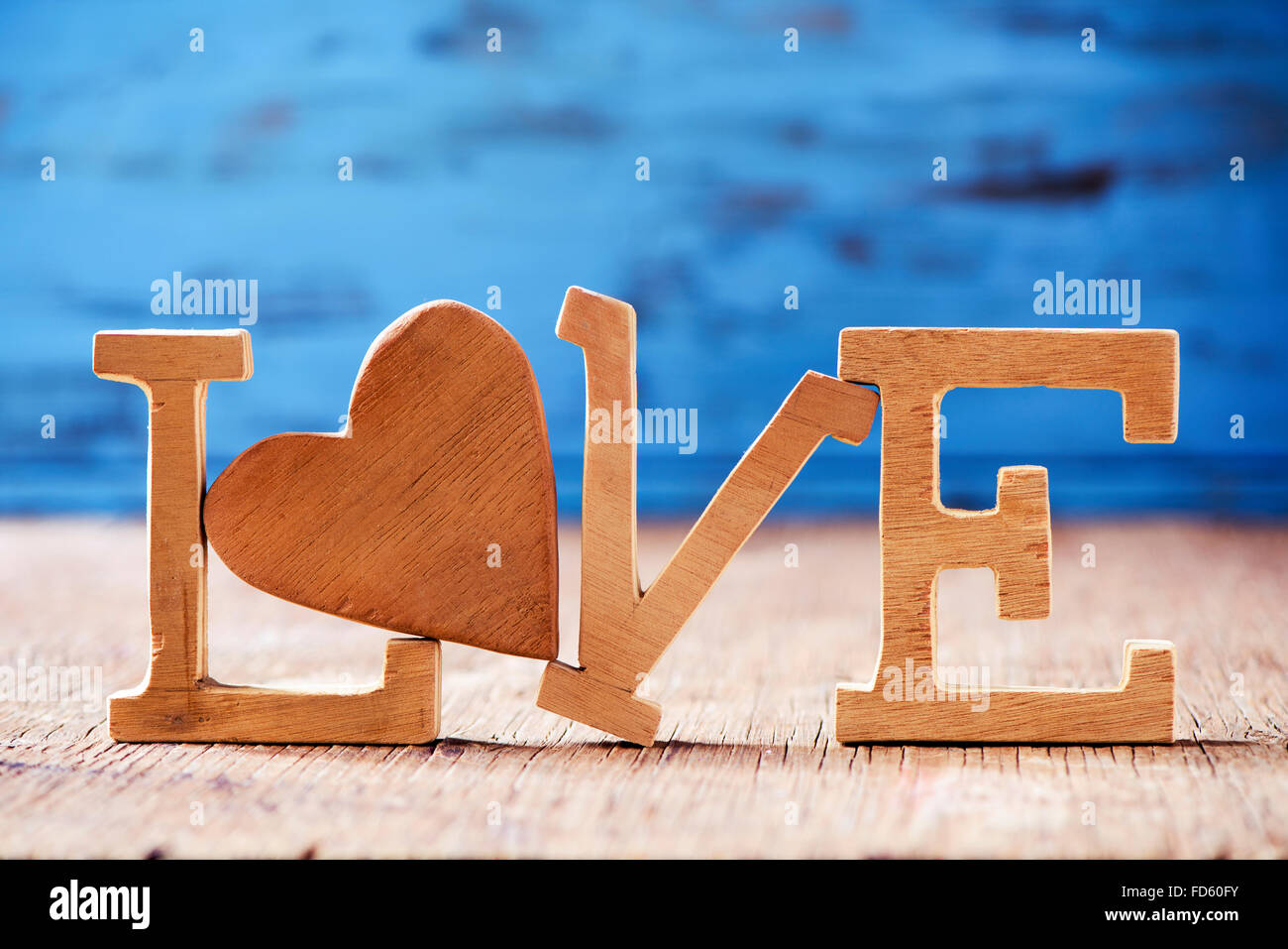 einige hölzerne Buchstaben bilden das Wort Liebe mit einem Herz aus Holz anstelle von den Buchstaben o im Hintergrund blau rustikal aus Holz Stockfoto
