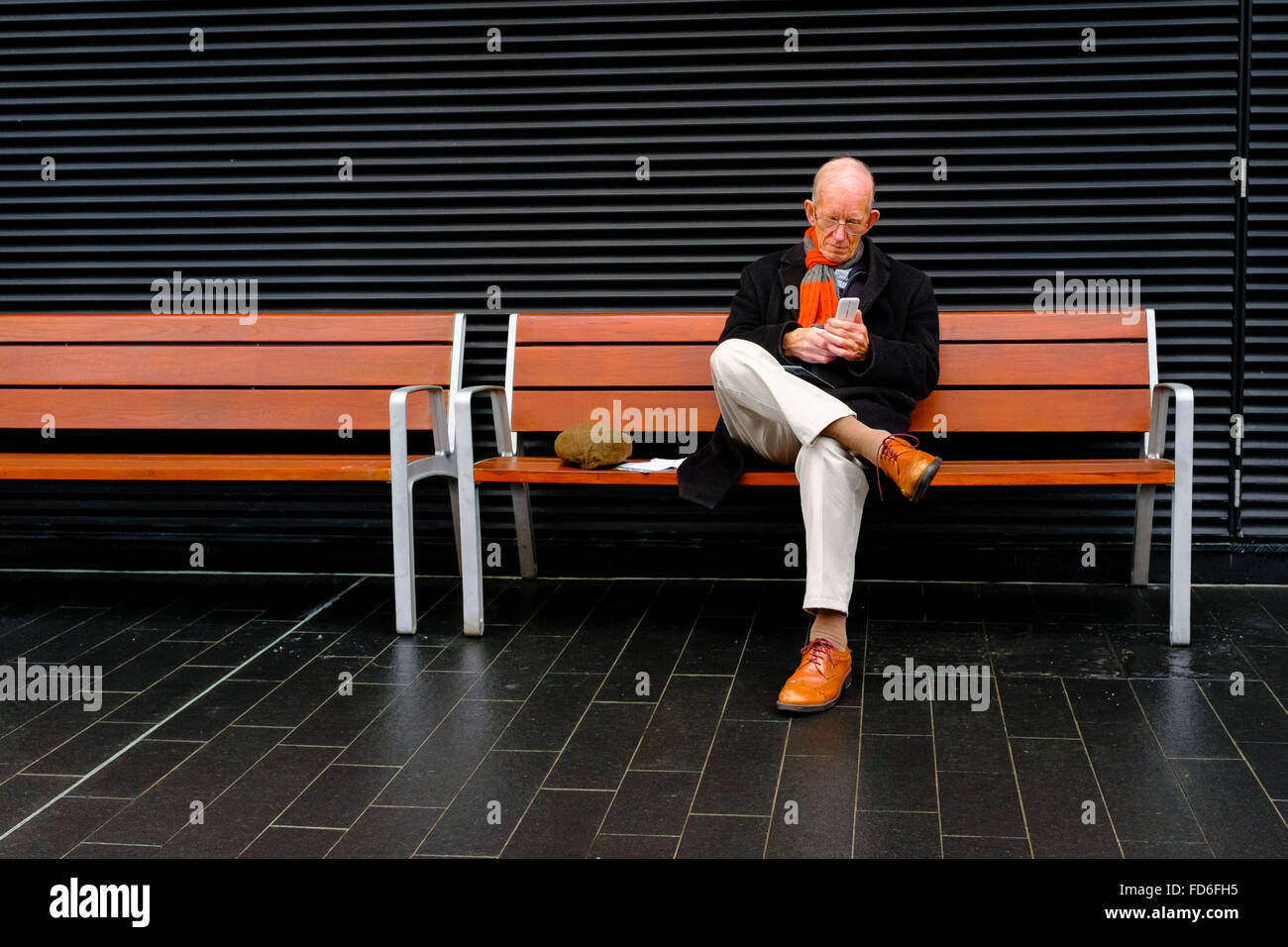 Ein reifer Mann, der Smartphone benutzt, während er auf einer öffentlichen Bank sitzt, London Stockfoto