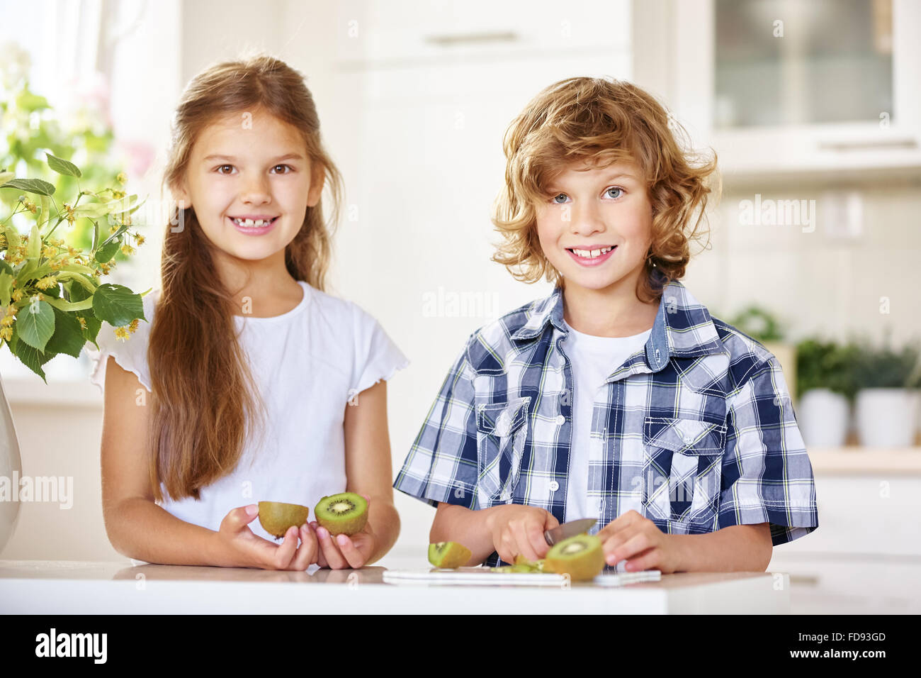 Zwei glückliche Kinder schneiden eine Kiwi in einer Küche Stockfoto
