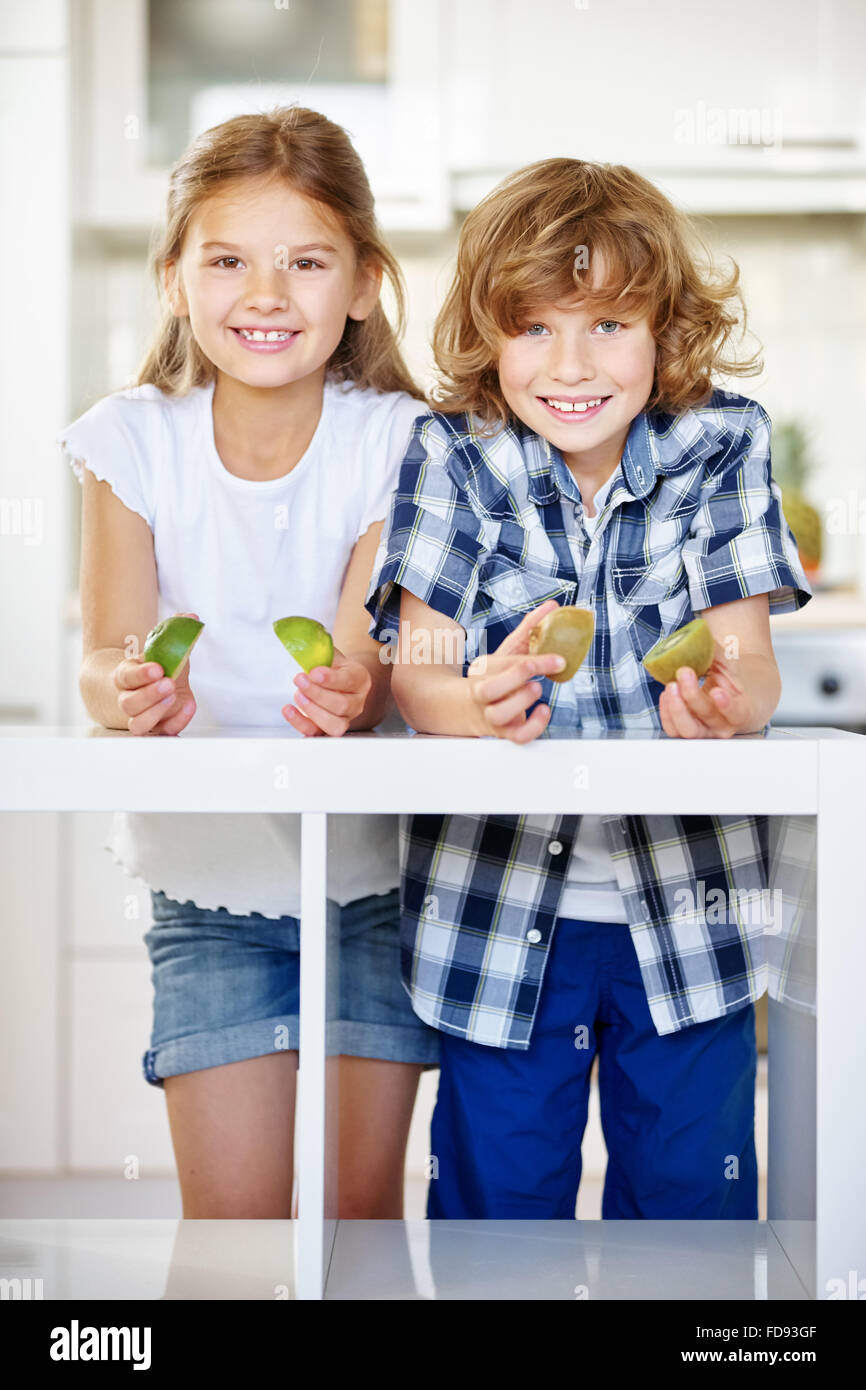 Zwei glückliche Kinder mit Kiwi-Hälften in der Küche Stockfoto
