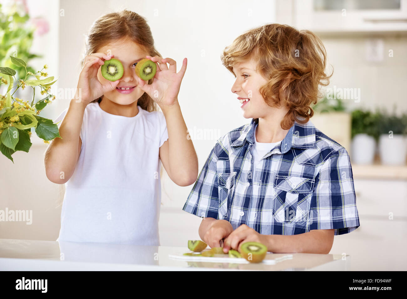 Zwei glückliche Kinder, die Spaß mit Kiwi in einer Küche Stockfoto