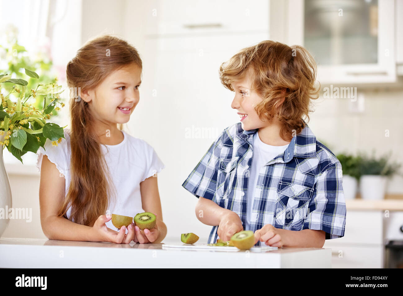 Zwei glückliche Kinder schneiden eine Kiwi für einen Obstsalat in der Küche Stockfoto