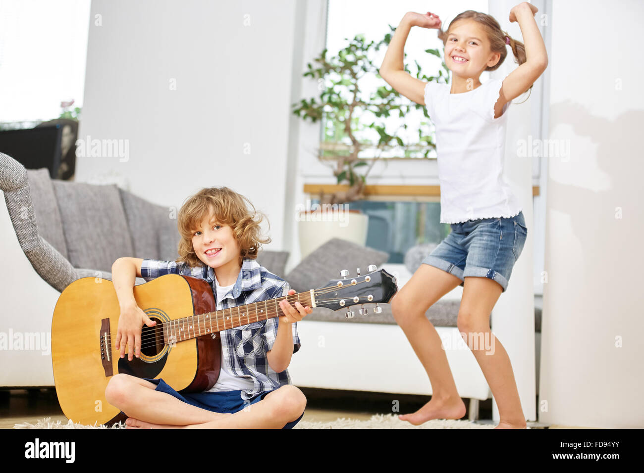 Mädchen tanzen zur Musik von jungen spielt die Gitarre zu Hause im Wohnzimmer Stockfoto