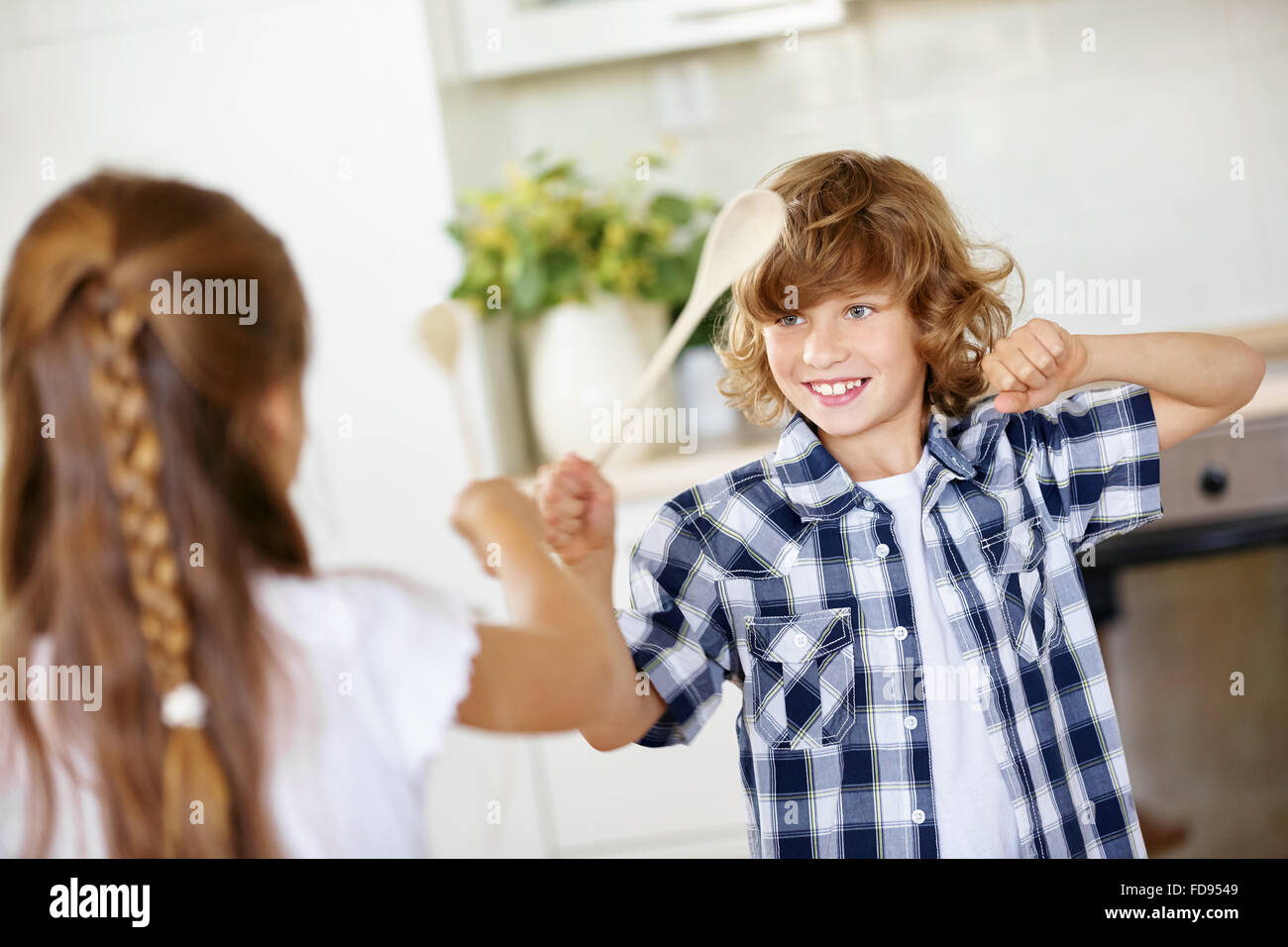 Zwei glückliche Kinder kämpfen im Scherz in Küche mit Holzlöffel Stockfoto