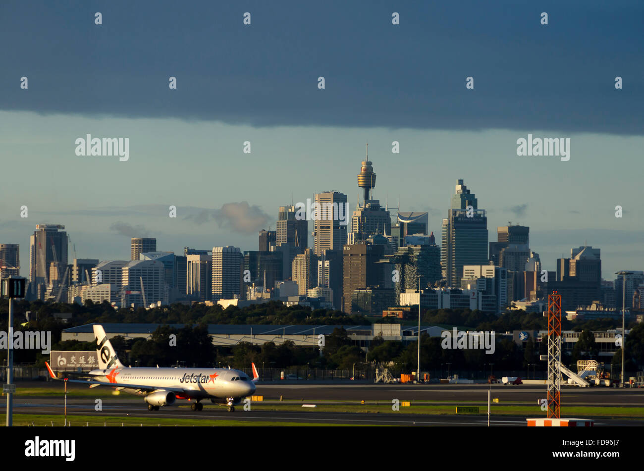 Jetstar Flugzeug landet auf dem Flughafen Kingsford Smith, CBD tower Gebäude in Distnace, Sydney, New South Wales, Australien Stockfoto