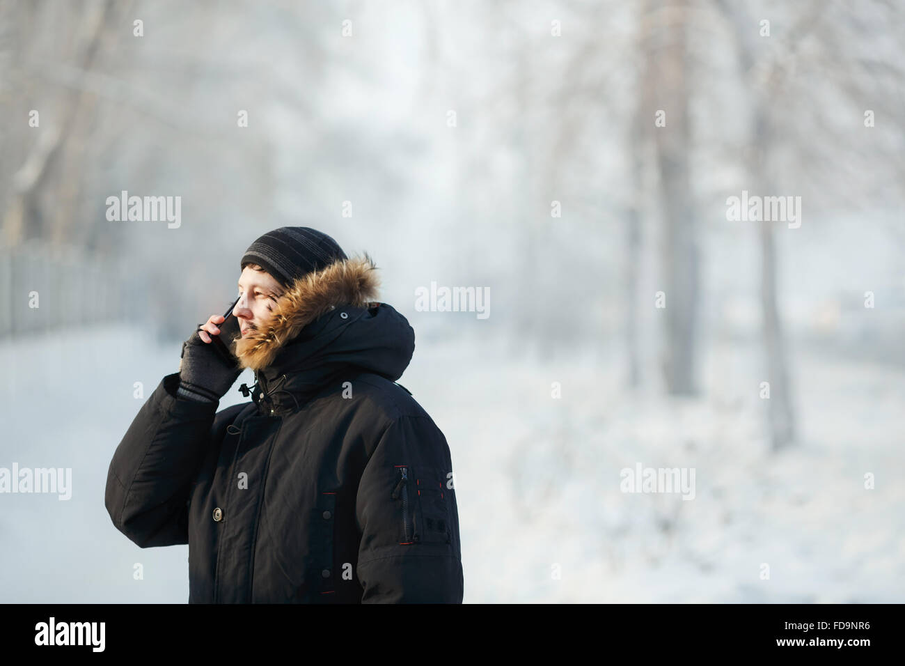 Sibirische Mann im Freien bei kalter Tag in einem warmen Winter Daunenjacke mit Fell Kapuze am Telefon zu sprechen. Schnee, Frost, Kommunikation bei jedem Wetter. Platz für Ihren Text. Stockfoto